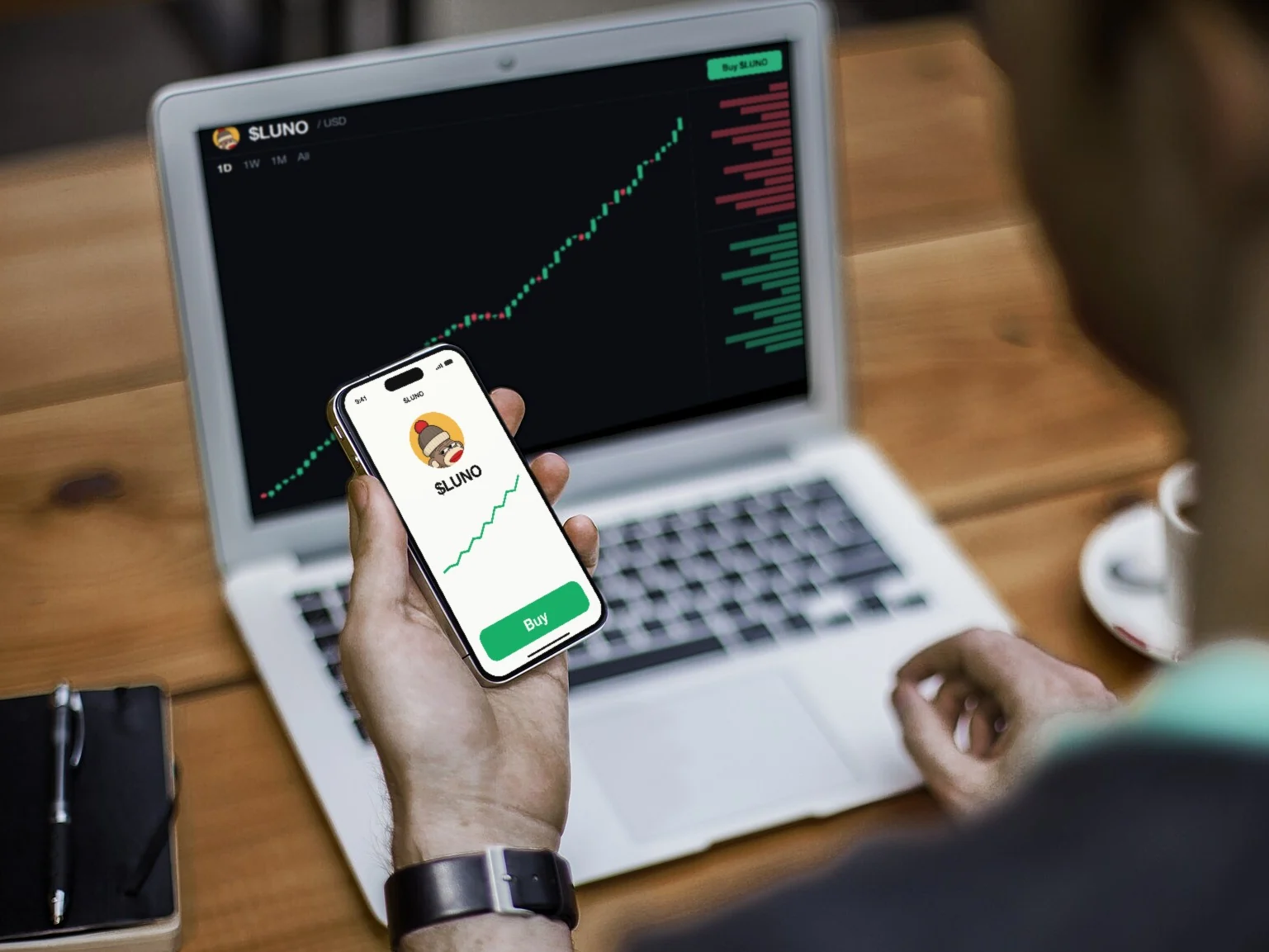 A laptop showing the $LUNO chart climbing, and an iPhone in his hand open on a Buy button